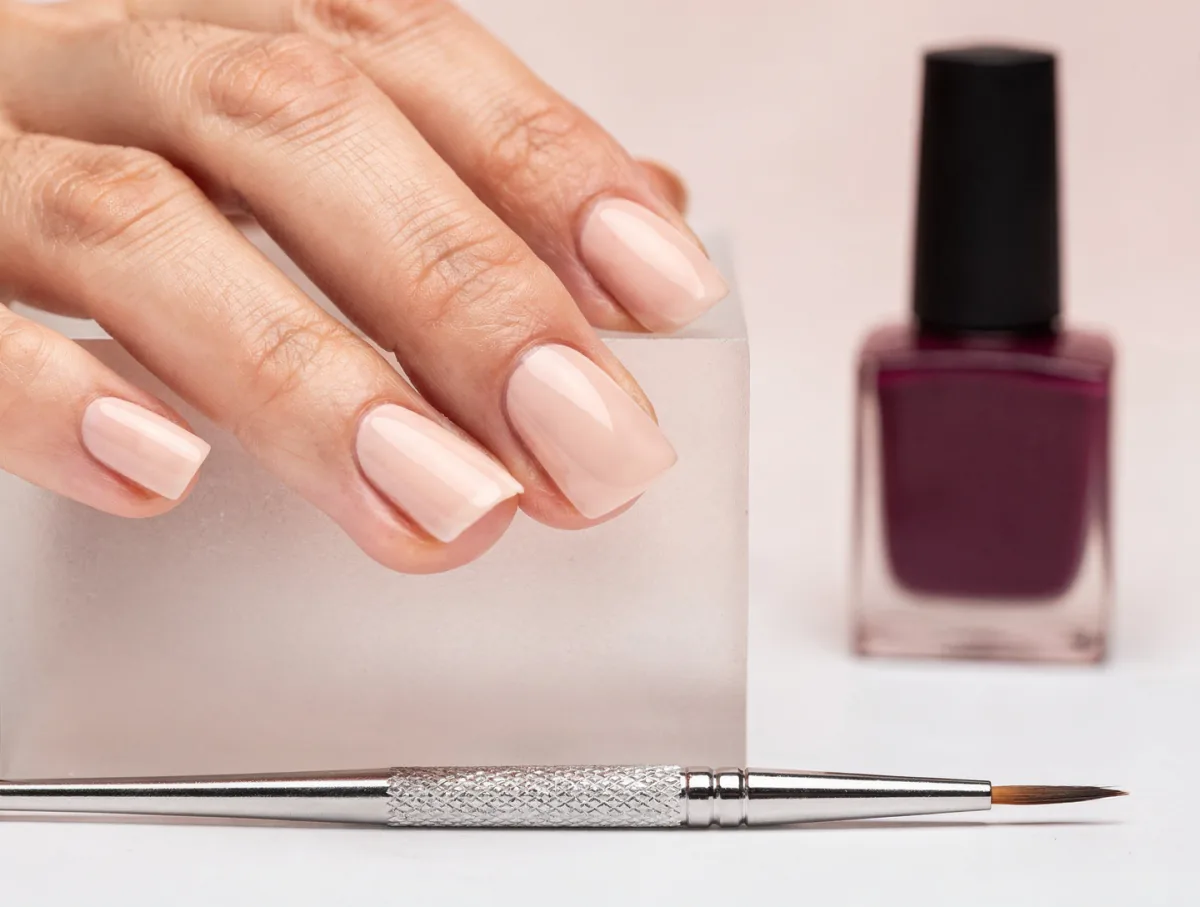Close-up of a finished almond nail set in milky blush beside a plum polish bottle