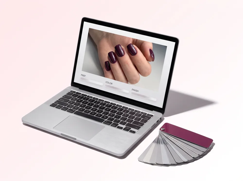 A laptop showing a manicure photograph and lesson progress beside a fan of chrome colour chips