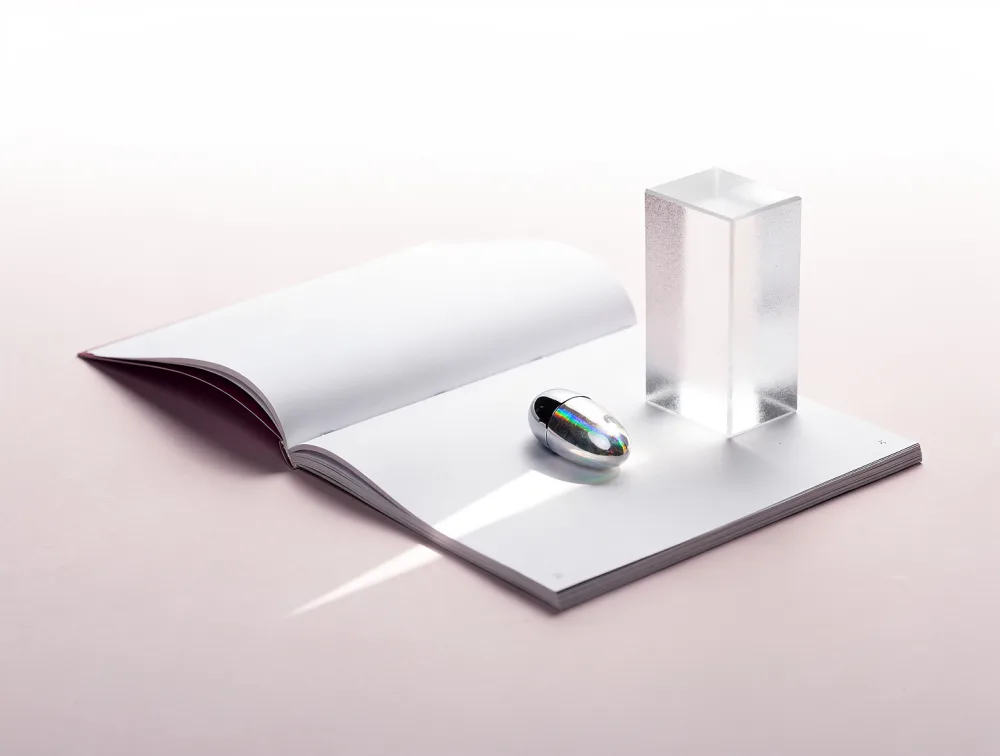 A magazine open at blank pages with a holographic nail sample and a prism of light